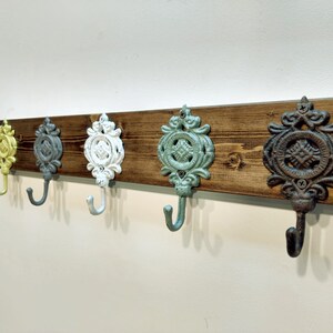 May include: A wooden wall-mounted coat rack with five decorative hooks. The hooks are cast iron and painted in various colours, including yellow, grey, white, teal, and brown.