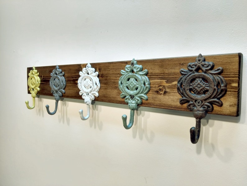 May include: A wooden wall-mounted coat rack with five decorative hooks. The hooks are cast iron and painted in various colours, including yellow, grey, white, teal, and brown.