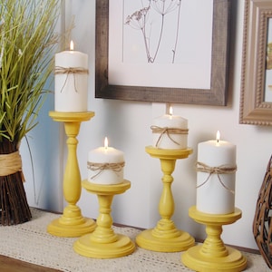 May include: Five yellow wooden candle holders with white candles on a table runner. The candles are tied with twine.