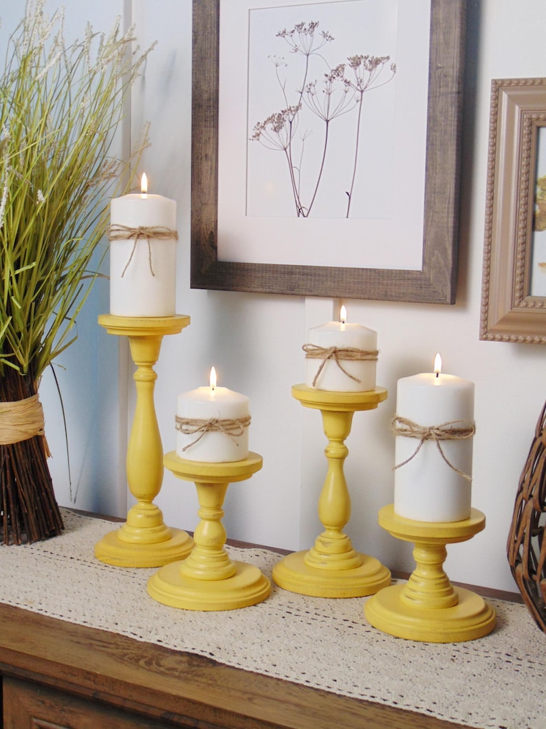 May include: Five yellow wooden candle holders with white candles on a table runner. The candles are tied with twine.