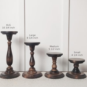 May include: Four wooden cake stands in different sizes. The stands are brown and have a distressed finish. The largest stand is 10 3/4 inches tall, the next largest is 8 1/4 inches tall, the medium stand is 5 1/2 inches tall, and the smallest stand is 4 1/4 inches tall.