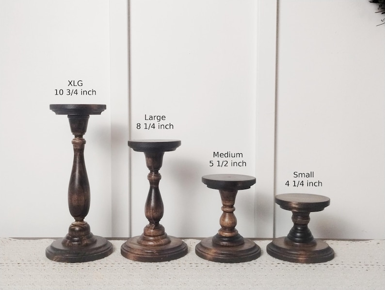 May include: Four wooden cake stands in different sizes. The stands are brown and have a distressed finish. The largest stand is 10 3/4 inches tall, the next largest is 8 1/4 inches tall, the medium stand is 5 1/2 inches tall, and the smallest stand is 4 1/4 inches tall.