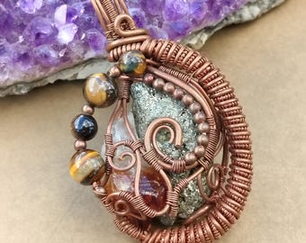 May include: A handcrafted copper wire pendant featuring a cluster of crystals and gemstones. The pendant includes a pyrite stone, tiger's eye beads, and a clear quartz crystal. The intricate wirework is wrapped around the stones, creating a unique, natural jewelry piece.