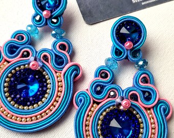 May include: A pair of handmade blue and pink soutache earrings with a central dark blue gemstone. The earrings feature intricate beadwork and a teardrop shape. The card in the background reads "SILK JEWELRY accessories".