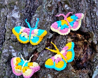 Puede incluir: Cuatro mariposas de ganchillo coloridas en amarillo, rosa y azul se muestran sobre un fondo de corteza de árbol texturizada. Cada mariposa tiene un patrón y una forma únicos, mostrando la artesanía. Estas mariposas decorativas son perfectas para añadir un toque caprichoso.