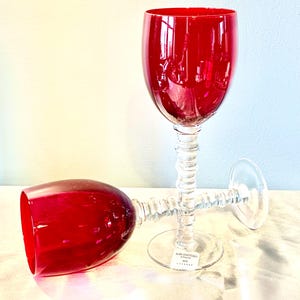 May include: Two red wine glasses. One is upright, the other is lying on its side. The glasses have a clear, textured stem and a round base. The bowl of the glasses is a deep red color.