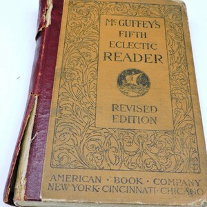 May include: An antique book titled "McGuffey's Fifth Eclectic Reader, Revised Edition." The cover is tan with black text and decorative flourishes. The spine is burgundy. The book is from the American Book Company, New York, Cincinnati, Chicago.