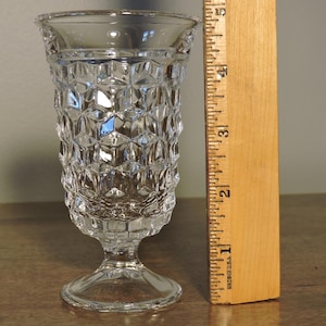 Peut inclure: Un vase en verre transparent de style vintage avec un motif g&eacute;om&eacute;trique textur&eacute;. Le vase mesure environ 10 cm de haut et poss&egrave;de un pied. Le bord a un bord d&eacute;coratif. Une r&egrave;gle en bois est &agrave; c&ocirc;t&eacute; du vase.