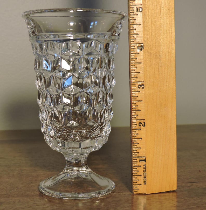 Peut inclure: Un vase en verre transparent de style vintage avec un motif g&eacute;om&eacute;trique textur&eacute;. Le vase mesure environ 10 cm de haut et poss&egrave;de un pied. Le bord a un bord d&eacute;coratif. Une r&egrave;gle en bois est &agrave; c&ocirc;t&eacute; du vase.
