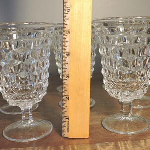 Peut inclure: Quatre verres &agrave; eau vintage transparents avec un motif g&eacute;om&eacute;trique textur&eacute;. Les verres mesurent environ 15 cm de haut et reposent sur une base ronde. Les gobelets sont en verre transparent et sont pr&eacute;sent&eacute;s sur une surface en bois.