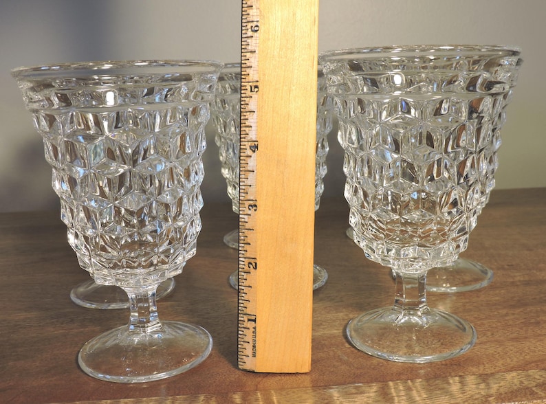 Peut inclure: Quatre verres &agrave; eau vintage transparents avec un motif g&eacute;om&eacute;trique textur&eacute;. Les verres mesurent environ 15 cm de haut et reposent sur une base ronde. Les gobelets sont en verre transparent et sont pr&eacute;sent&eacute;s sur une surface en bois.