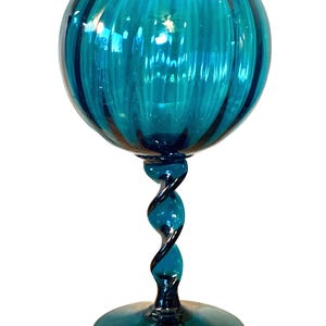 Peut inclure: Un gobelet en verre de couleur teal avec un bol rond et une tige torsadée. Le bol présente des rainures verticales et un bord festonné. La tige est noire et teal, et la base est un cercle plat. Le verre a une finition brillante.