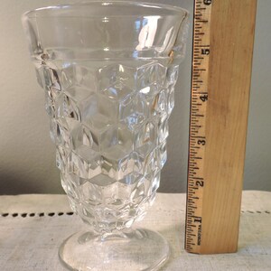 Peut inclure: Verre clair avec un design g&eacute;om&eacute;trique &agrave; facettes. Le verre a une base ronde et un bord &eacute;vas&eacute;. Une r&egrave;gle en bois est plac&eacute;e &agrave; c&ocirc;t&eacute; du verre, mesurant environ 15 cm de hauteur.
