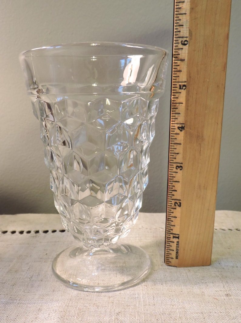 Peut inclure: Verre clair avec un design g&eacute;om&eacute;trique &agrave; facettes. Le verre a une base ronde et un bord &eacute;vas&eacute;. Une r&egrave;gle en bois est plac&eacute;e &agrave; c&ocirc;t&eacute; du verre, mesurant environ 15 cm de hauteur.