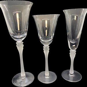 May include: Three clear crystal wine glasses with etched designs. The glasses have a frosted, leaf-like design on the stems and a delicate, etched pattern on the bowls. The glasses are of varying sizes, with a tall, slender champagne flute on the right.