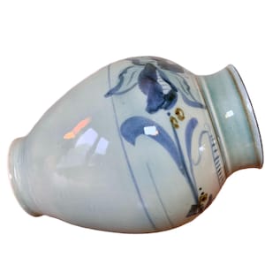May include: A ceramic vase with a light blue and white glaze. The vase features a floral design in dark blue and gold. The rim is a light green color. The vase is a decorative item.