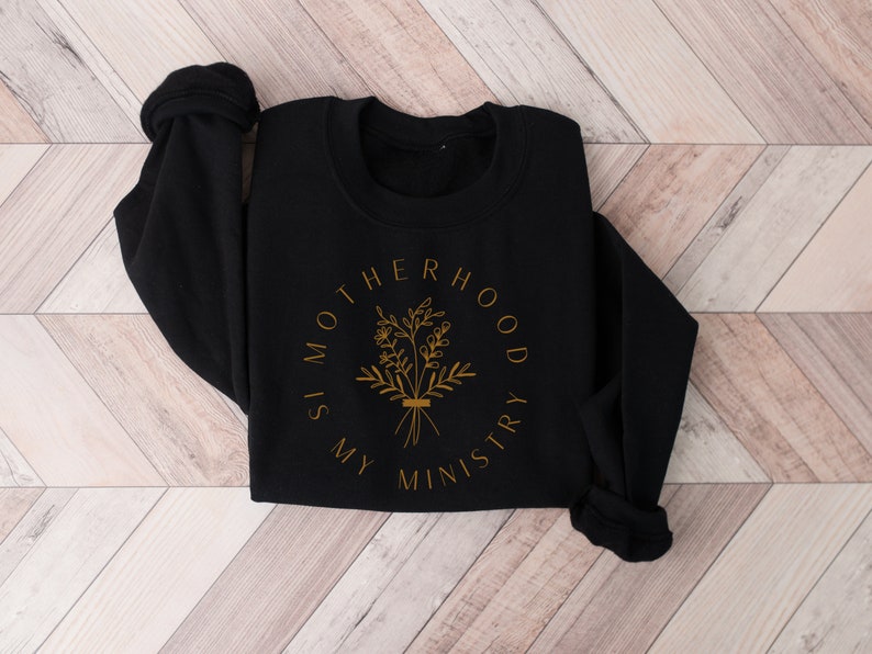 May include: Black sweatshirt with a gold graphic that reads "Motherhood is my ministry" with a floral design.