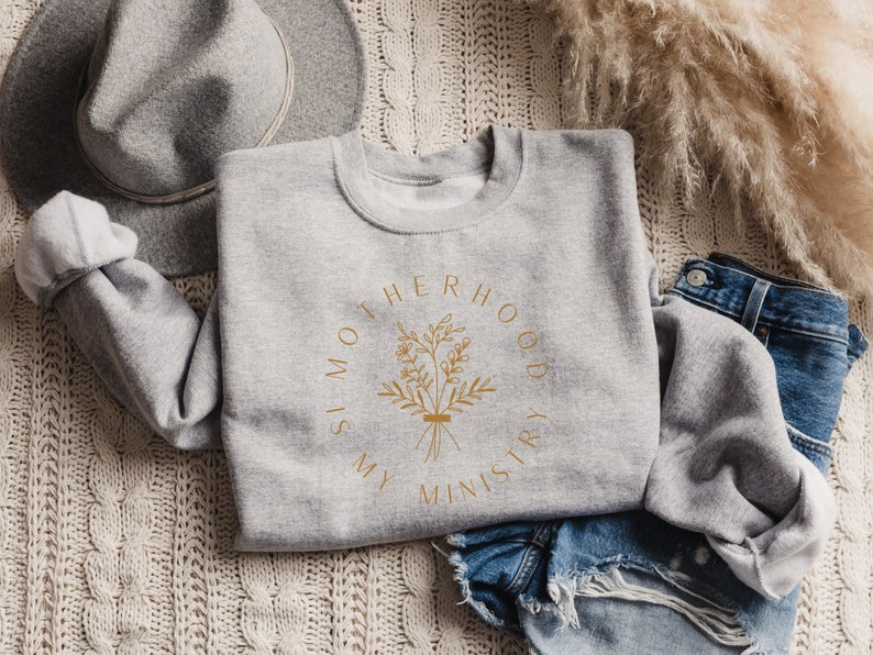 May include: Gray sweatshirt with a gold graphic that says "Motherhood is my ministry" with a floral design.