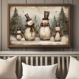 Op de afbeelding: Een ingelijst schilderij van een sneeuwpopfamilie die in een besneeuwd bos staat. De sneeuwpoppen dragen hoeden en sjaals en houden mokken vast. Het schilderij heeft een rustieke, vintage stijl.