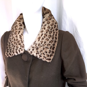 May include: A brown coat with a leopard print collar. The coat has two large buttons and long sleeves. The collar is a light brown with dark brown spots. The coat is displayed on a mannequin.