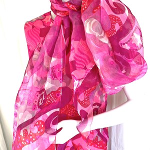 以下が含まれることがあります： 鮮やかなホットピンク、マゼンタ、ライトピンクの色合いの抽象的なパターンが特徴のノースリーブトップスとスカーフ。生地は半透明で軽量であり、デザイン全体に有機的な形状、ドット、曲線が描かれています。