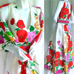 Puede incluir: Un vestido blanco y un chal a juego con estampado floral. El vestido presenta un cuello halter y una falda amplia, ceñida a la cintura con un cinturón rosa y verde. El chal tiene cuello en V y mangas largas. El estampado floral incluye amapolas rojas, flores rosas y hojas verdes.