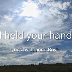 May include: Image of a bright blue sky filled with fluffy white clouds. The text "I held your hand" is displayed in white, with "Lyrics by Joanne Boyle" below.