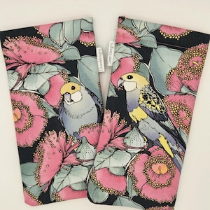 May include: Two fabric eyeglass cases with a colourful floral and bird design. The cases feature a black background with pink flowers, green leaves, and illustrations of yellow, grey, and blue birds. The brand name "Deasldesigns" is printed on a white tag.