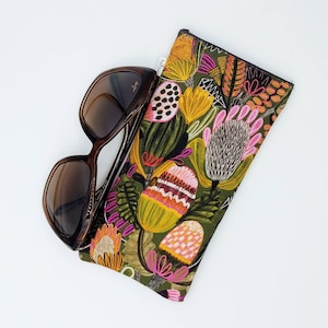 May include: A brown and black sunglasses case with a floral print featuring pink, yellow, and green flowers. The case is made of fabric and has a zipper closure.
