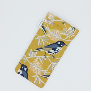 May include: A yellow fabric glasses case with a white bird and flower pattern. The case has a white label with the text "DownUnderDesigns".