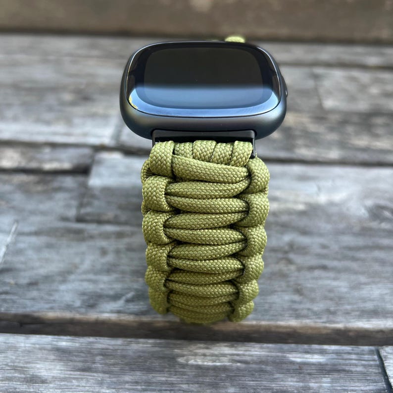 May include: A green paracord watch band for a smartwatch. The band is made of woven paracord and has a black buckle.