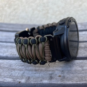 May include: A black smartwatch with a brown and black paracord strap. The watch has a round face and a black bezel.