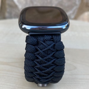 May include: A black smartwatch with a black woven paracord strap. The watch face is black and has a silver bezel.