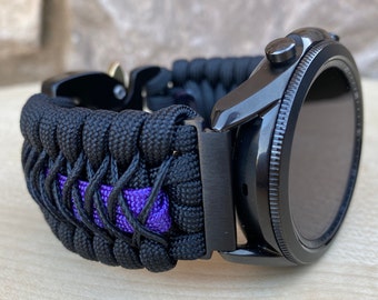 May include: Black smartwatch with a woven black and purple paracord band. The watch has a black bezel and a digital display. The band is made of durable, braided nylon cord, and the watch is designed for everyday wear.