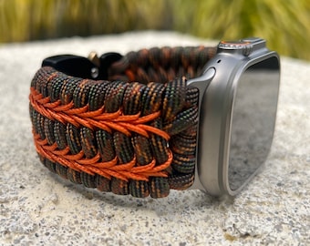 May include: A camouflage and orange paracord watch band for an Apple Watch.