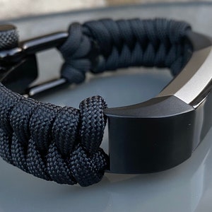 May include: A black fitness tracker with a black paracord band and a silver metal clasp.