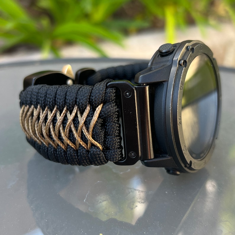 May include: Black and tan paracord watch band with a black watch face. The watch band is woven with a criss-cross pattern.