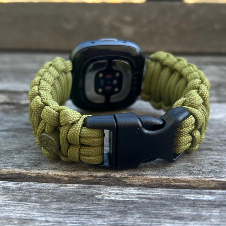 May include: A green paracord watch band with a black buckle. The band is made of woven paracord and has a secure clasp.