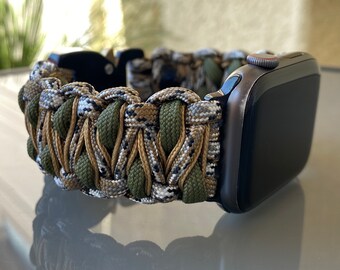 Op de afbeelding: Een zwarte Apple Watch met een groene, bruine en witte camouflage paracord band.