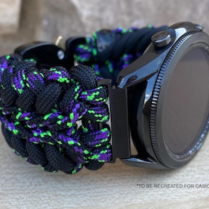 Puede incluir: Reloj inteligente negro con una correa trenzada en negro, morado y verde neón. El reloj tiene un bisel negro y una pantalla oscura. La correa está hecha de cuerda gruesa y tejida. El texto en la parte inferior dice "*TO BE RECREATED FOR CASIO WATCH."