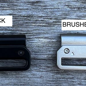 May include: Two metal belt buckle options: one black and one brushed metal. Both buckles have a rectangular shape with a cut-out in the center.