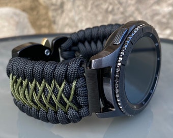 May include: Black smartwatch with a black and green paracord strap. The watch has a rotating bezel and a black face.