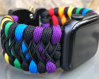 Puede incluir: Un Apple Watch negro con una banda de paracord arcoíris. La banda está hecha de paracord negro, morado, azul, verde, amarillo, naranja y rojo.