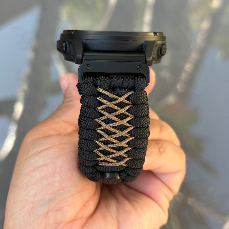 May include: Black and tan paracord watch band with a black watch face.