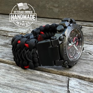 Puede incluir: Reloj G-Shock negro con una correa de paracord negra y roja. La esfera del reloj tiene detalles rojos y una pantalla digital. La correa está hecha a mano en los EE. UU.