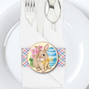 May include: A white napkin with a blue, pink, and yellow plaid ribbon around it. The ribbon has a round sticker with a cartoon bunny holding a blue and white striped Easter egg.