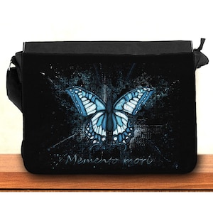 May include: Black canvas messenger bag with a blue butterfly graphic and the text "Memento mori" in white.
