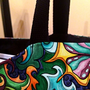 May include: A colorful tote bag with black handles. The bag features a swirling pattern of green, blue, yellow, orange, and pink.