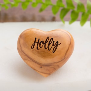 Puede incluir: Un corazón de madera en forma de corazón con el nombre "Holly" grabado en él. El corazón está hecho de madera marrón claro y tiene un patrón de veta natural.