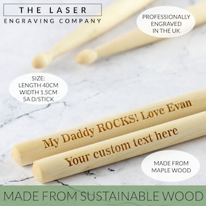 Puede incluir: Dos baquetas de madera con grabados personalizados. La baqueta superior dice "My Daddy ROCKS! Love Evan". La baqueta inferior dice "Your custom text here". Ambas baquetas est&aacute;n hechas de madera de arce y miden 40 cm de largo y 1,5 cm de ancho.